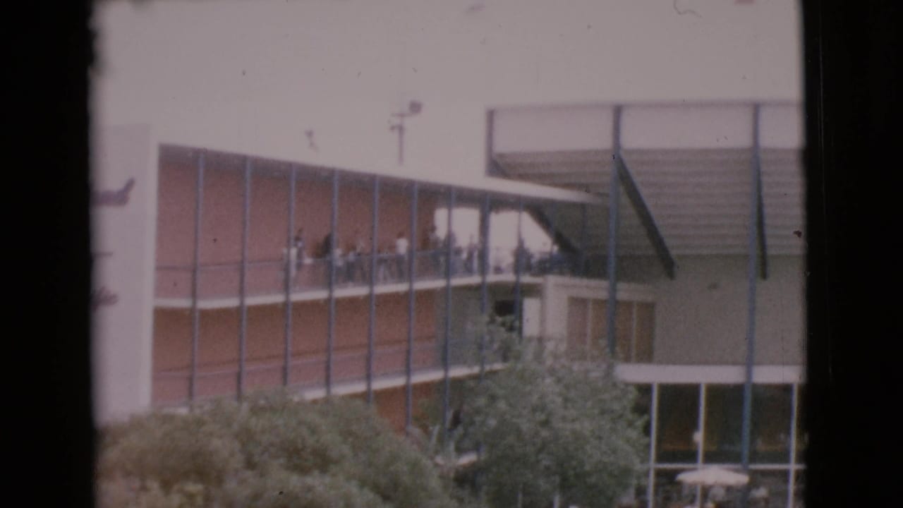 1968 home-movie frame showing visitors on a MarineLand balcony above trees and lower courtyard windows.