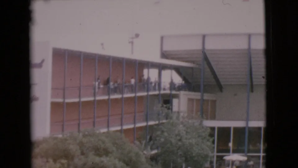 1968 home-movie frame showing visitors on a MarineLand balcony above trees and lower courtyard windows.