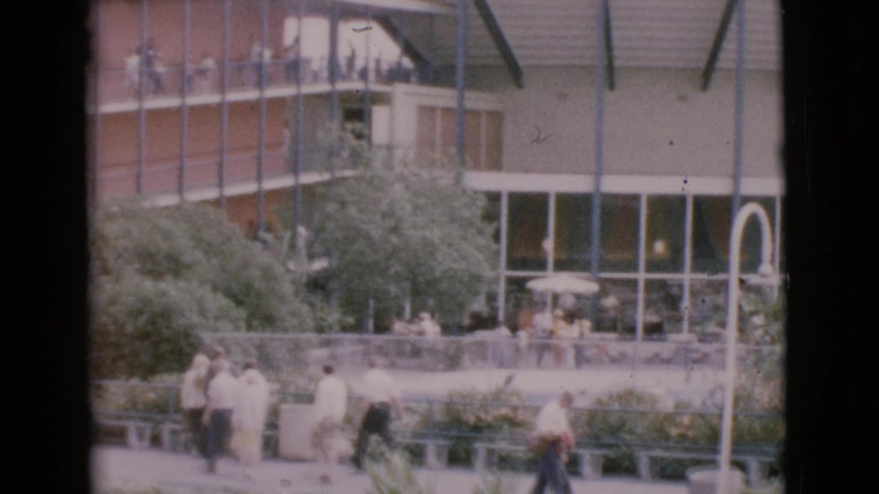 Pedestrians walk through a landscaped courtyard in front of a glass-fronted modern building.