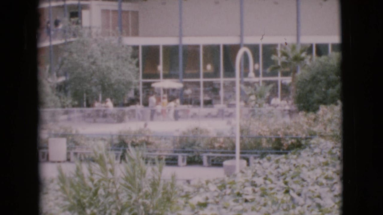 San Diego County 1968 courtyard scene with seated and walking figures, dense landscaping, benches, curved lighting, and a modern glass facade.