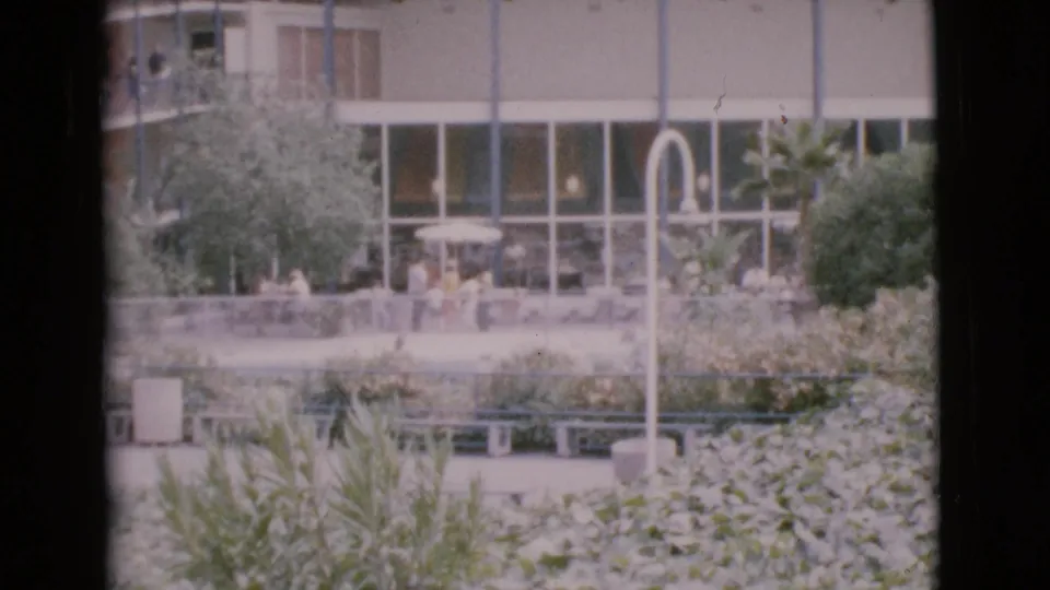 San Diego County 1968 courtyard scene with seated and walking figures, dense landscaping, benches, curved lighting, and a modern glass facade.