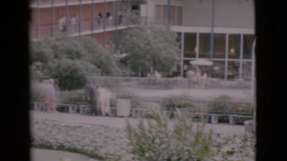 Visitors in a landscaped Southern California courtyard appear near benches and plantings outside a glass-fronted attraction building.