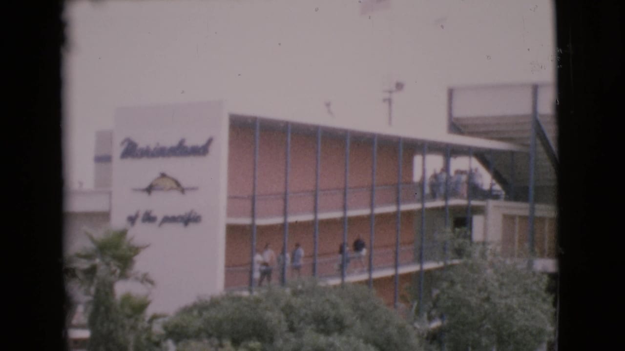 1968 frame showing a Marineland of the Pacific sign on a modern building, with visitors visible along an exterior balcony.