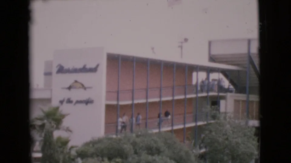 1968 frame showing a Marineland of the Pacific sign on a modern building, with visitors visible along an exterior balcony.