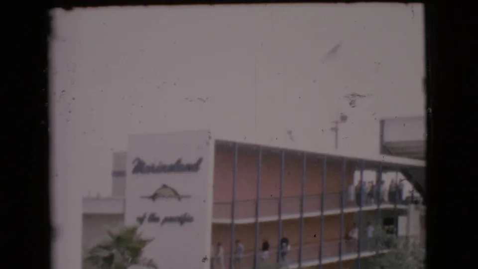 1968 San Diego County home-movie frame with Marineland signage, penguins by the pool, and small visitor figures on the building walkway.