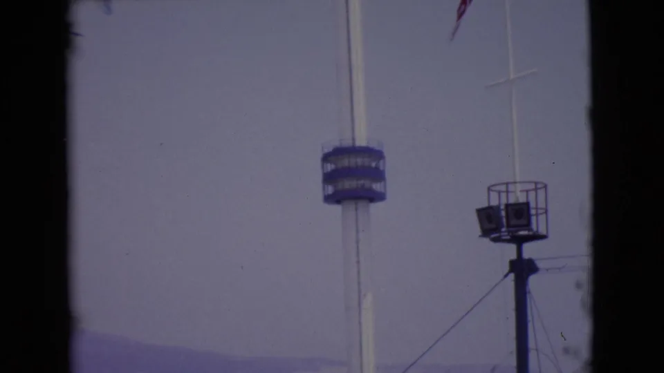 1968 San Diego County frame with a tall white pole, blue circular platform, raised speaker or light stand, and hazy sky.