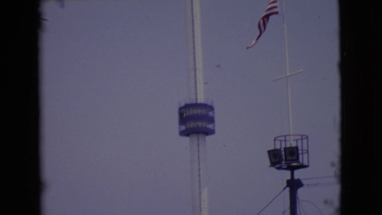 1968 San Diego County 8mm frame showing the American flag above a blue tower platform and a raised speaker or light stand.