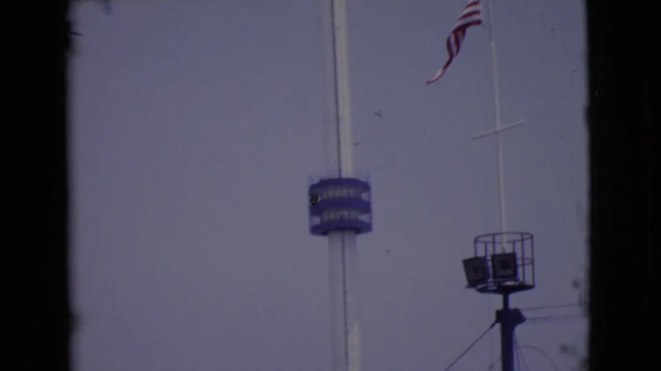 1968 San Diego County 8mm frame showing the American flag above a blue tower platform and a raised speaker or light stand.