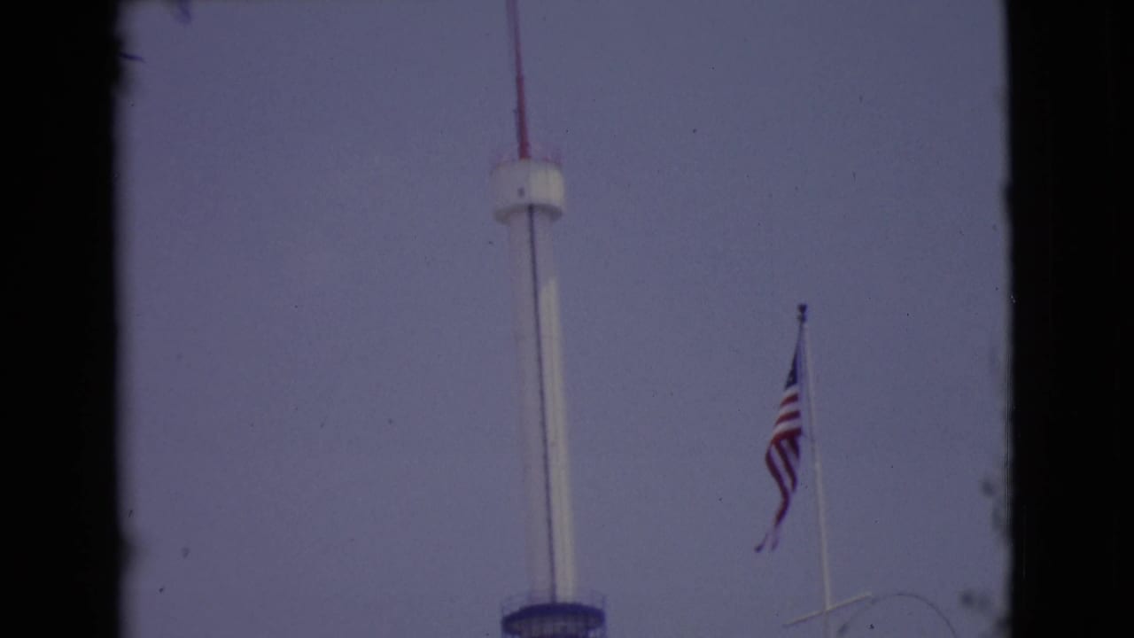 The upward pan continues on the tall white pole, with the blue deck low in frame and an American flag to the right.