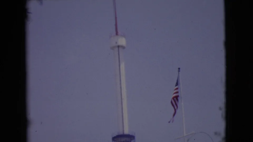The upward pan continues on the tall white pole, with the blue deck low in frame and an American flag to the right.