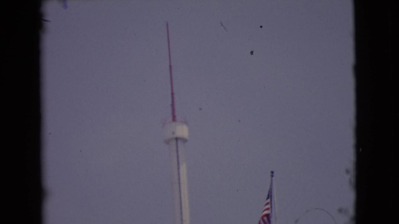 White observation tower with red antenna and partial American flag against a pale sky.
