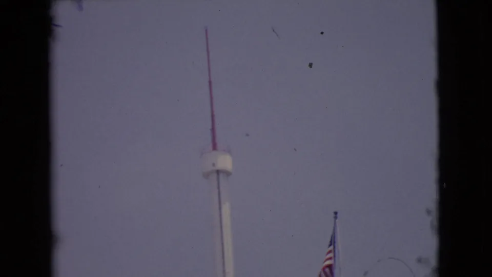 1968 San Diego County 8mm frame showing a white observation tower, red antenna, and partial American flag at the edge of the shot.