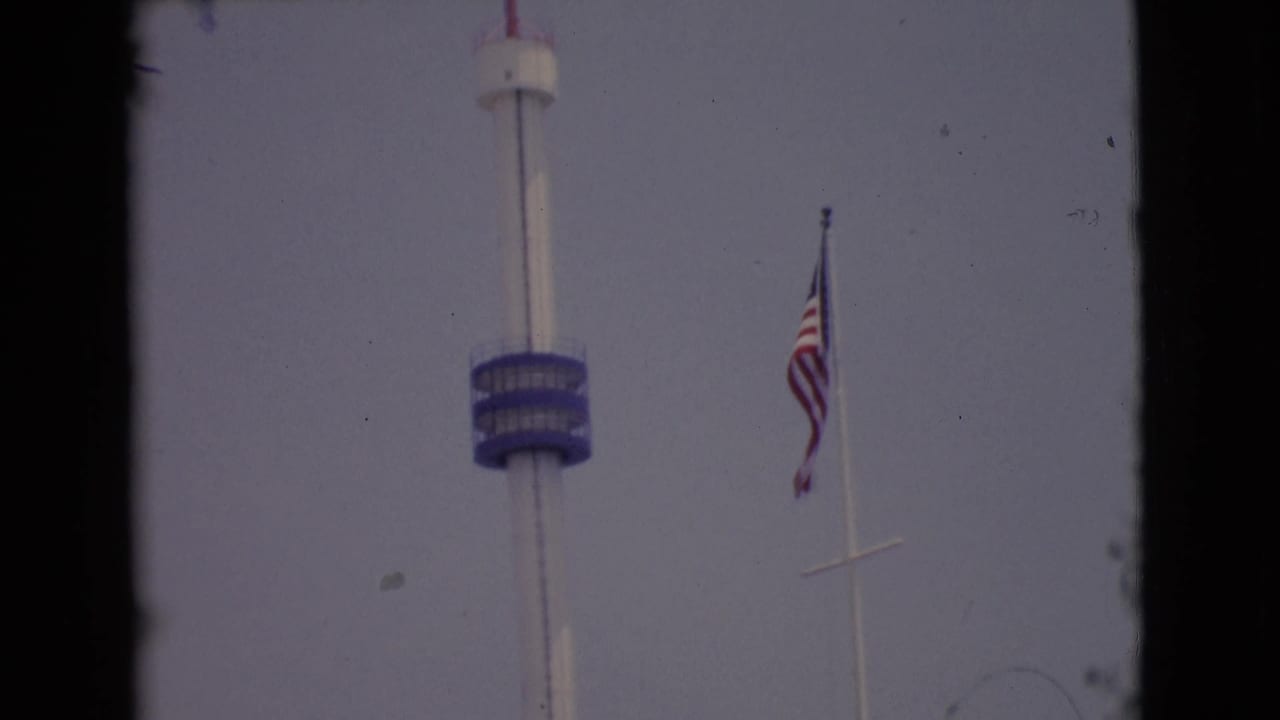 1968 San Diego County 8mm frame showing the blue-decked observation tower and American flag from a handheld visitor viewpoint.