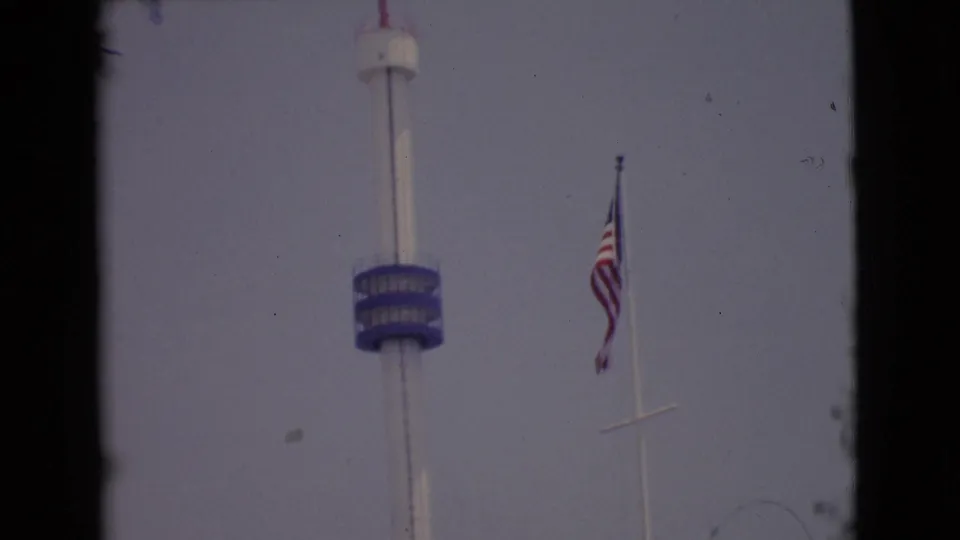 1968 San Diego County 8mm frame showing the blue-decked observation tower and American flag from a handheld visitor viewpoint.