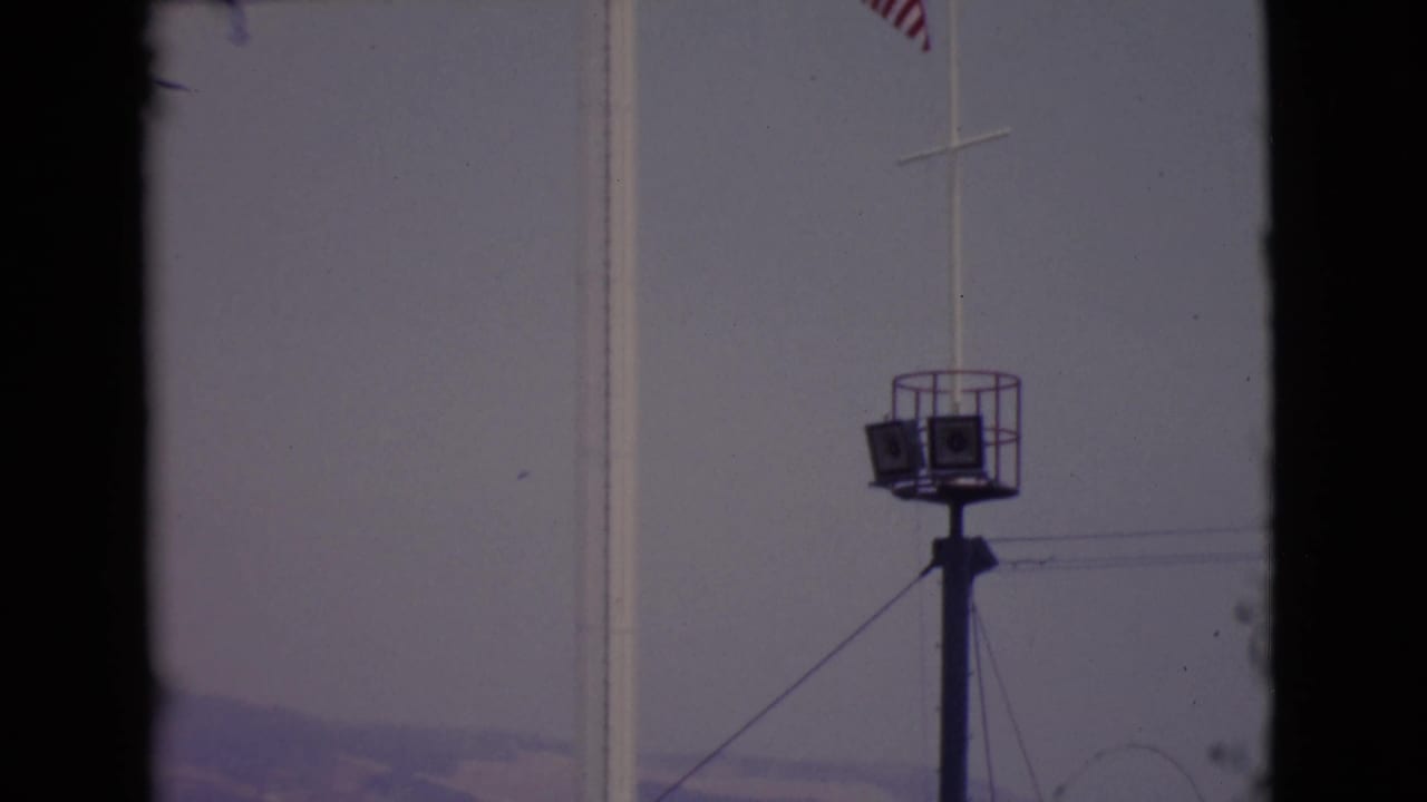 1968 San Diego County 8mm frame with the tower, flagpole, distant hills, and a small elevated platform or light structure.
