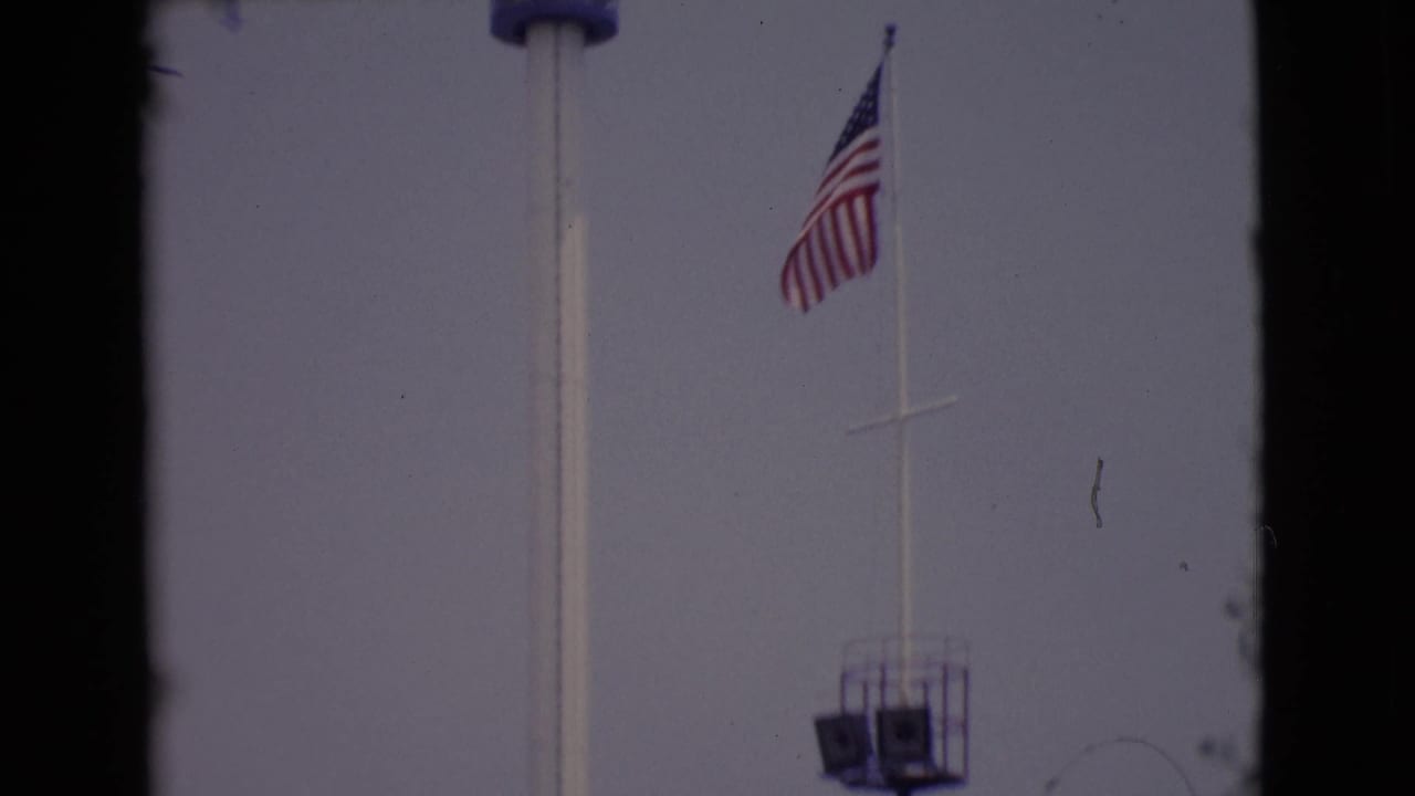 American flag and partial tower seen through dark window framing against a pale sky.