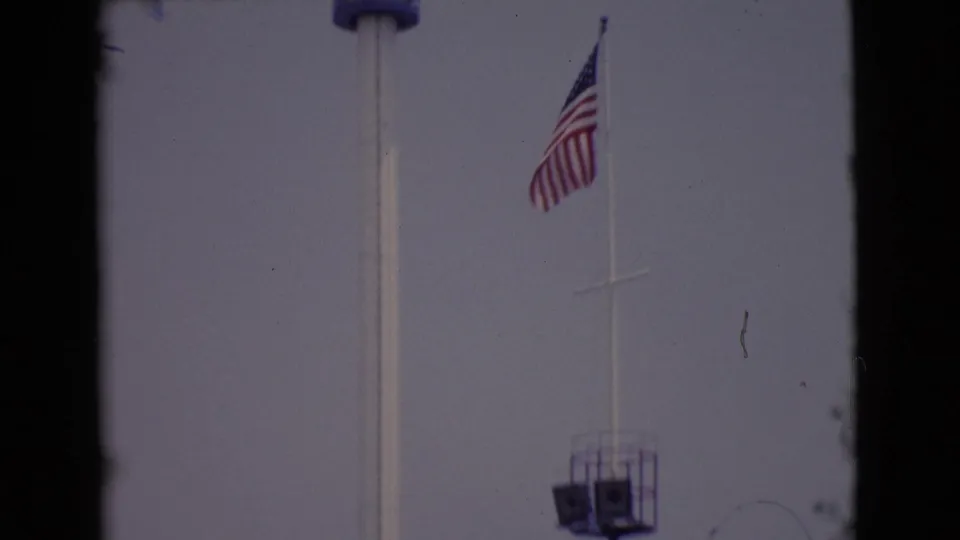 1968 San Diego-area 8mm frame showing a U.S. flag and part of a tower viewed through dark window edges.