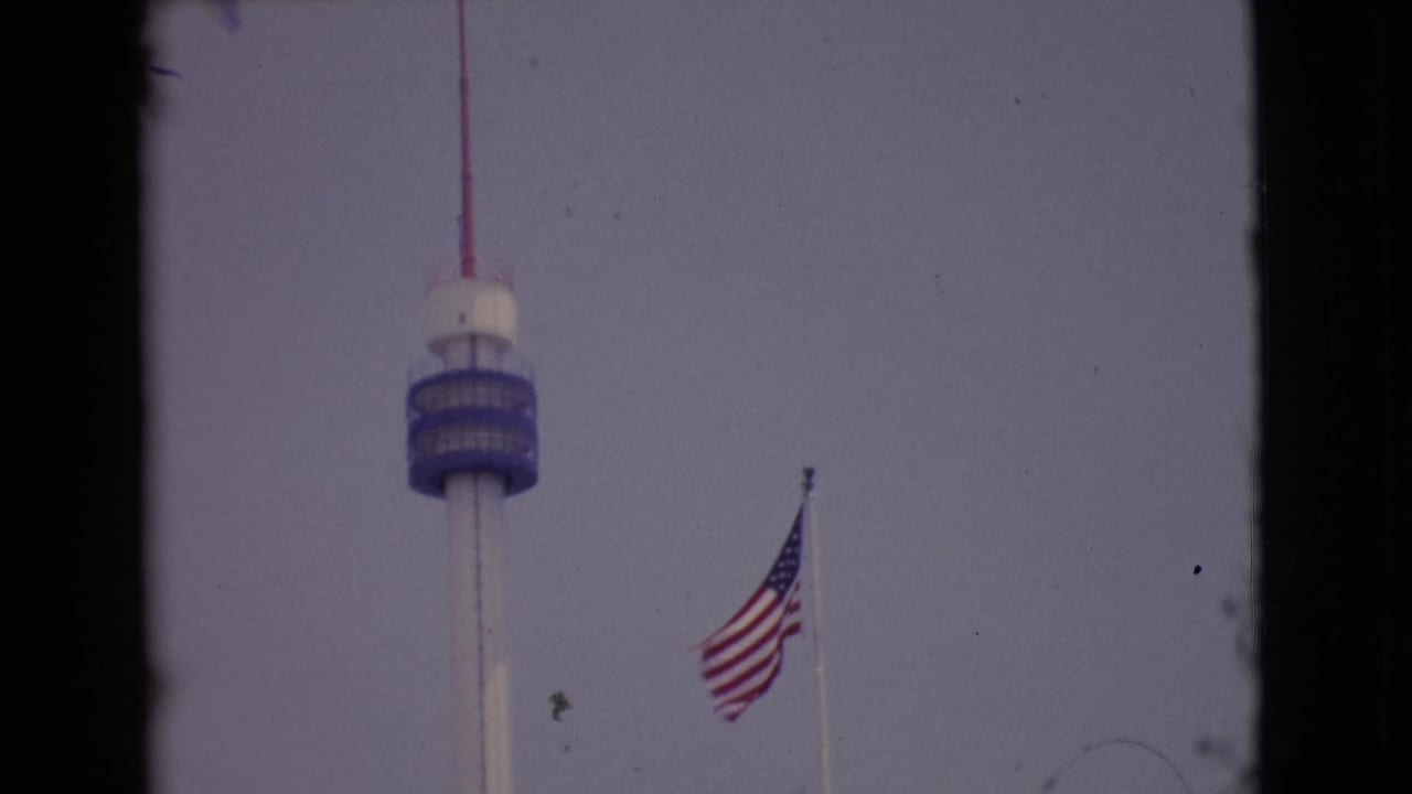 U.S. flag waving near a tall tower against a pale sky.