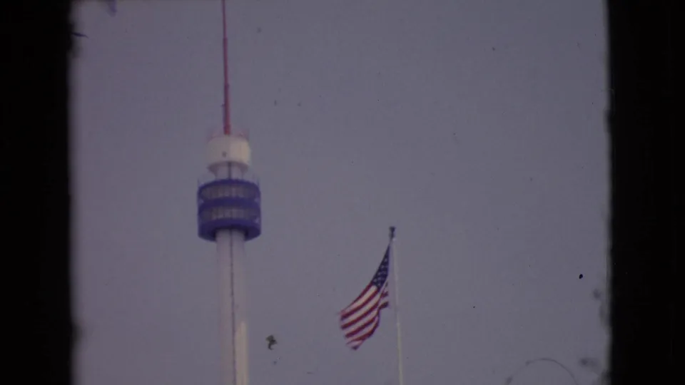 1968 San Diego County 8mm frame showing a U.S. flag below a tall tower with dark film borders.