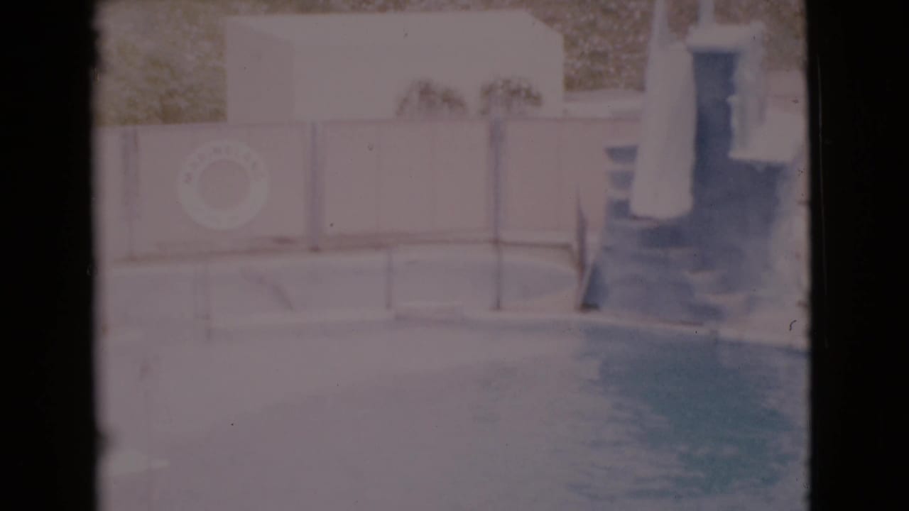 1968 San Diego County poolside view with blue water, a white safety ring mounted on the wall, potted plants, and steps at the right edge.