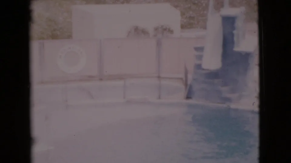 1968 San Diego County poolside view with blue water, a white safety ring mounted on the wall, potted plants, and steps at the right edge.