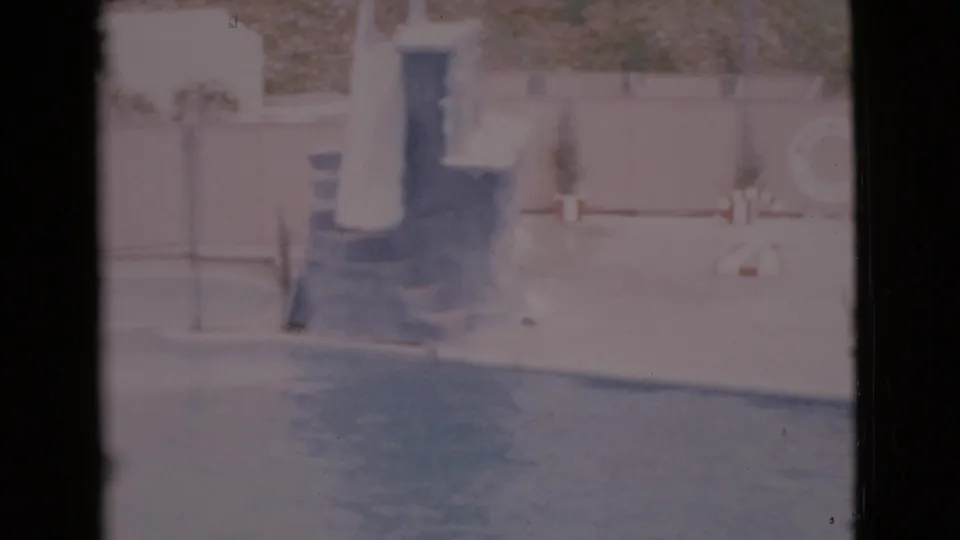 Faded 1968 home-movie frame of an outdoor pool deck in San Diego County, with steps, potted plants, a pale wall, and water along the bottom.
