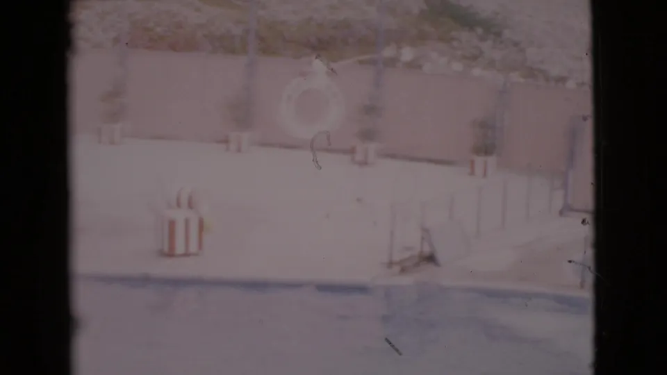 Faded 1968 San Diego County home-movie frame of a poolside area with a life ring, deck furniture, and low railing.