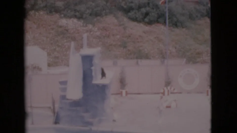 1968 San Diego County home-movie frame of a seal-show platform, pool edge, staff figure, and circular sign.