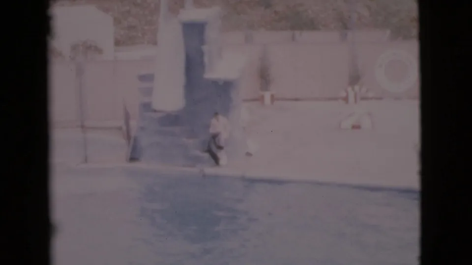 Faded 1968 San Diego County frame with a seal moving toward the pool below a platform and a trainer figure near the wall.