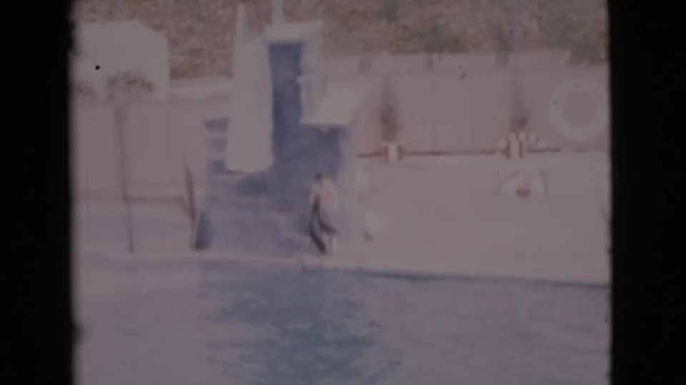 Faded 8mm frame from the San Diego County clip showing the seal entering the pool with a trainer beside the wall.