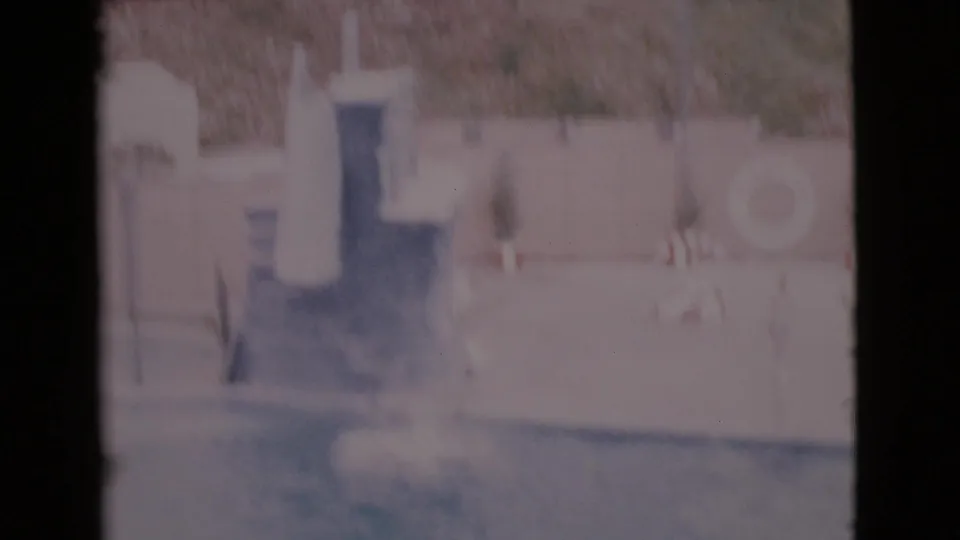 Soft, overexposed 1968 San Diego County frame showing the pool after the dive, with a trainer figure and wall in view.