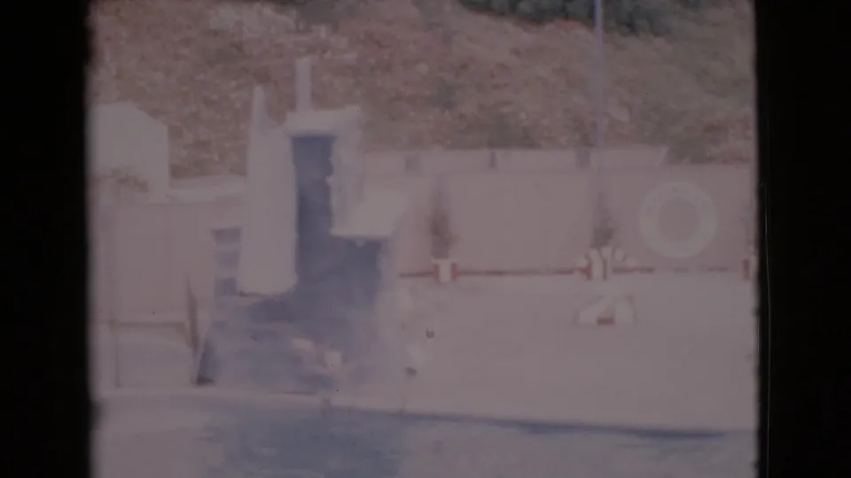 1968 San Diego County 8mm frame showing an empty swimming pool area with a diving board, life preserver, low fence, and hillside.