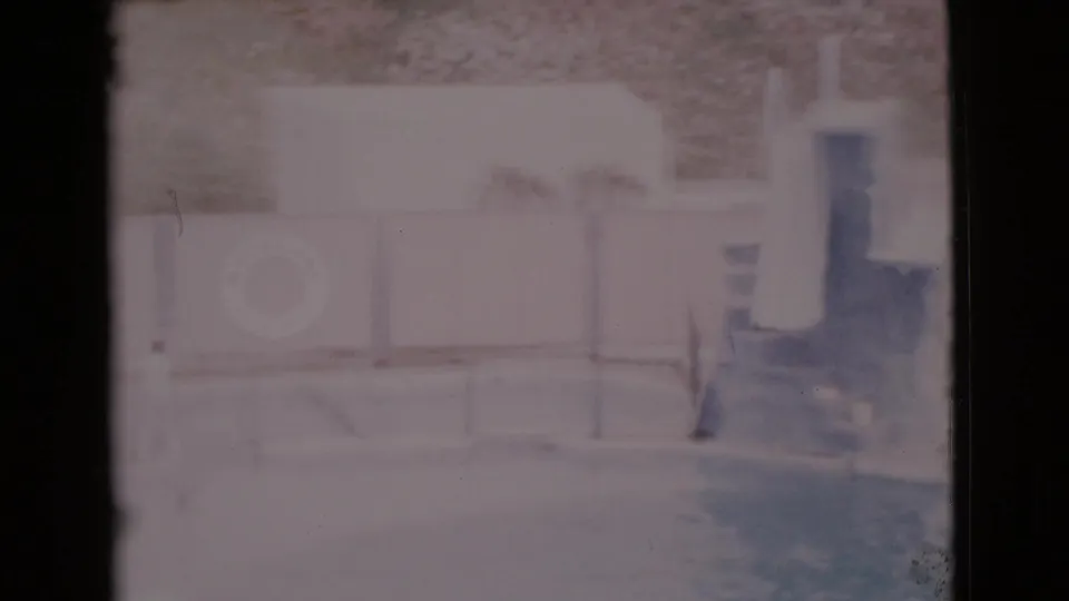 1968 San Diego County home-movie view of a quiet pool area, showing a life ring, diving board, low fencing, and pale poolside walls.