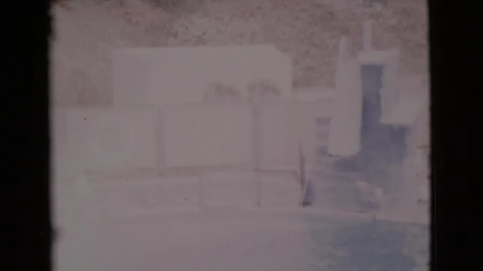 Soft 1968 San Diego County pool-area frame with an empty deck, low fence, wall-mounted life preserver, and hillside background.