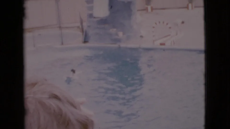 Faded 8mm frame from San Diego County showing a foreground blond-haired person and a dark moving shape on the water.