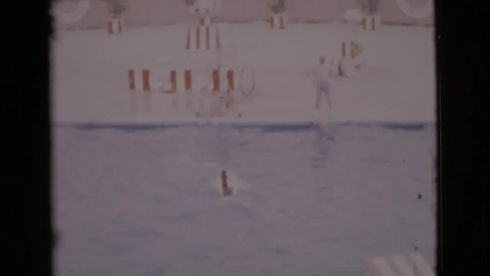 1968 San Diego County home-movie frame showing a dog in a pool during a water act, with hoop props and a deckside person visible.
