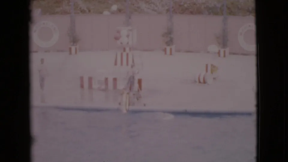 1968 San Diego 8mm frame showing a dolphin near a red-and-white hoop with a trainer on the pool deck.