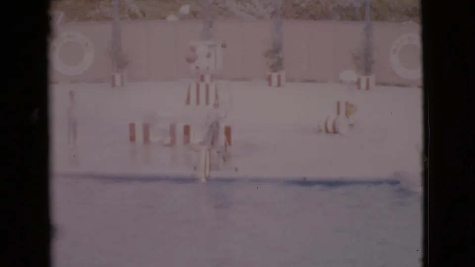 1968 San Diego home-movie frame of a trainer and dolphin beside a striped hoop at a public aquatic show.