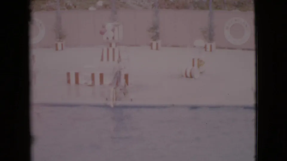 Soft 8mm view of a San Diego County dolphin show area with a trainer, hoop equipment, barriers, and pool water.
