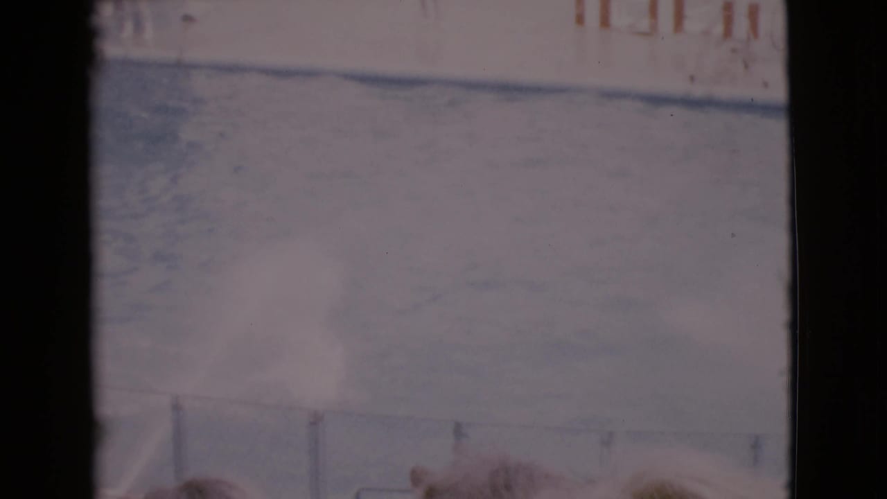 1968 San Diego County home-movie frame showing a sunlit marine show pool with railings and faint signage in soft, faded color.