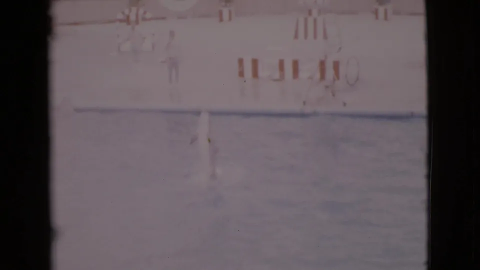 Faded 1968 8mm frame of a dolphin jumping from a marine-park pool in San Diego County, with deck markings in the background.