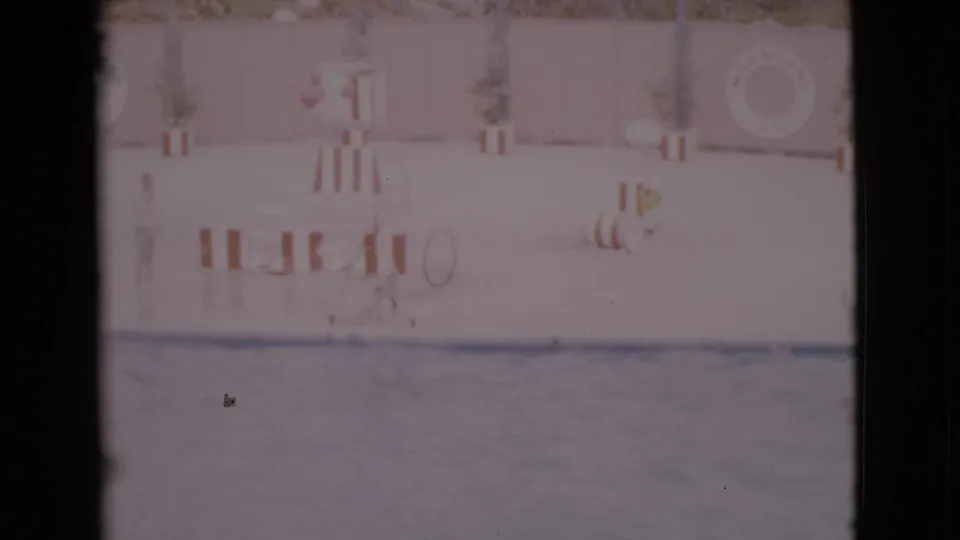 Soft 8mm frame from a 1968 San Diego County marine show, with pool water and striped deck barriers visible.