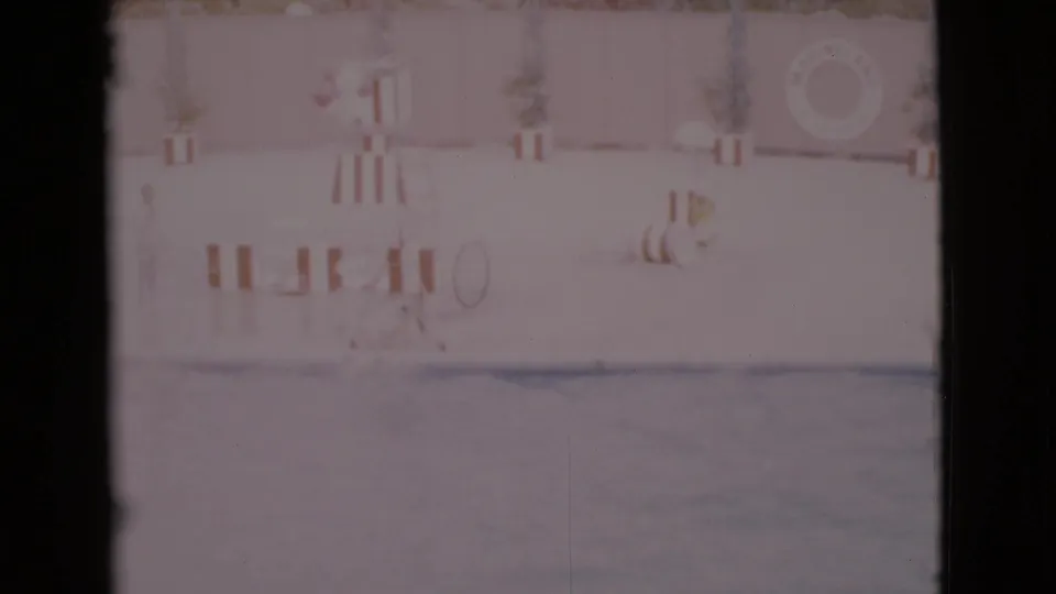 1968 San Diego County home-movie frame of a dolphin jumping above an aquatic park pool with deck fixtures and signage behind it.