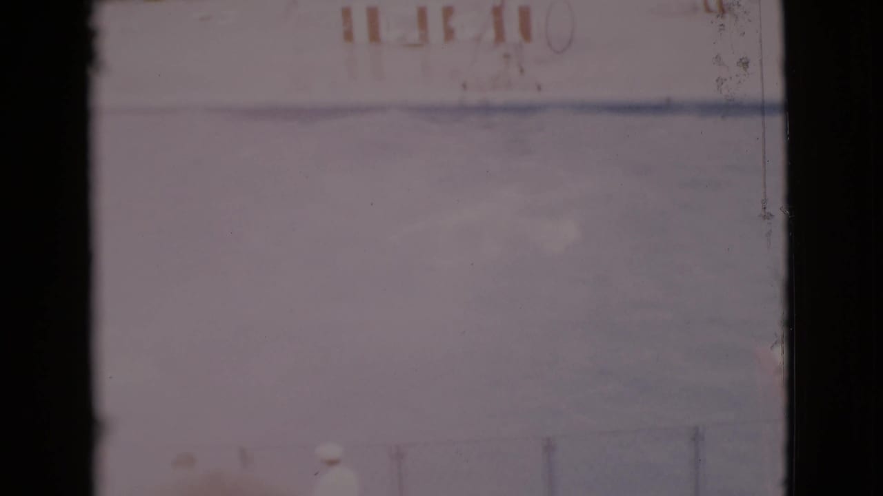 Faded 8mm frame showing a bright pool area with dark film borders and faint structures beyond the water.
