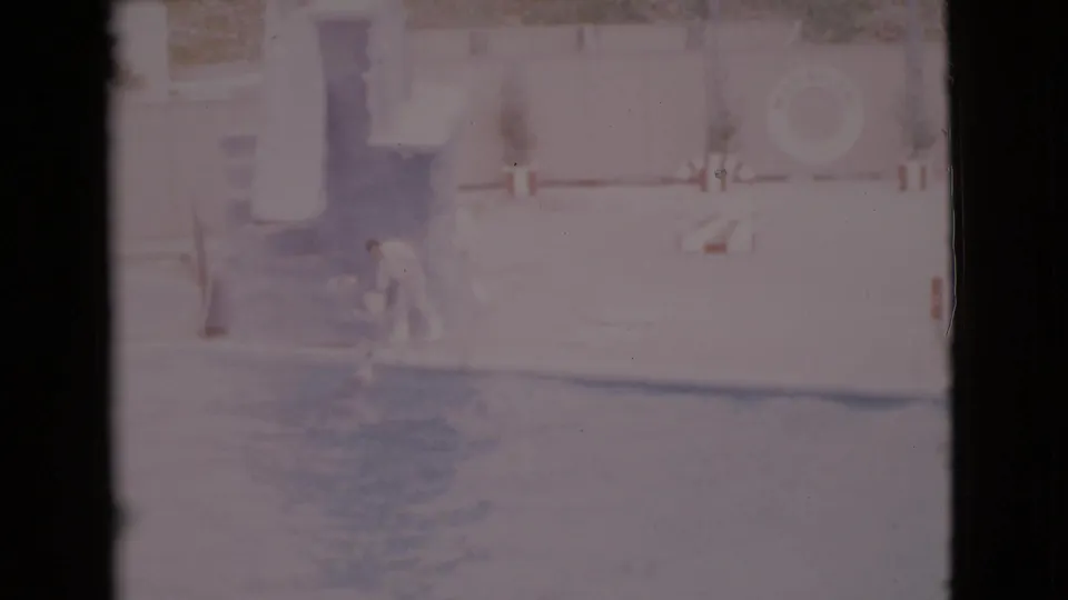 1968 San Diego County home-movie frame showing a person at a marine pool edge as dolphins appear near the surface.