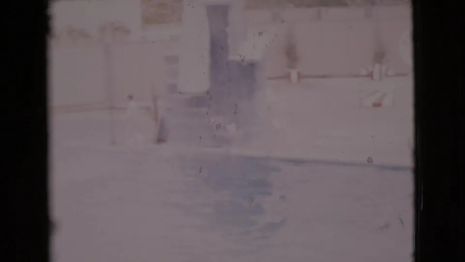1968 San Diego County home-movie frame showing a person by a marine pool as dolphins pass through faded blue water.