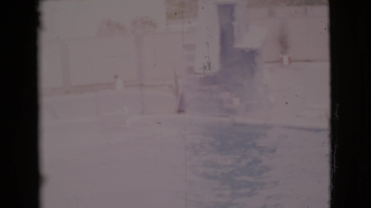 Soft, overexposed view of an outdoor pool area with buildings and shadows in the background.
