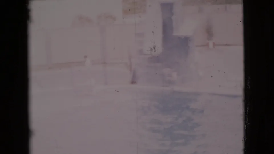 1968 San Diego County 8mm frame showing a faded, overexposed outdoor pool area with pale structures and dark poolside shadows.