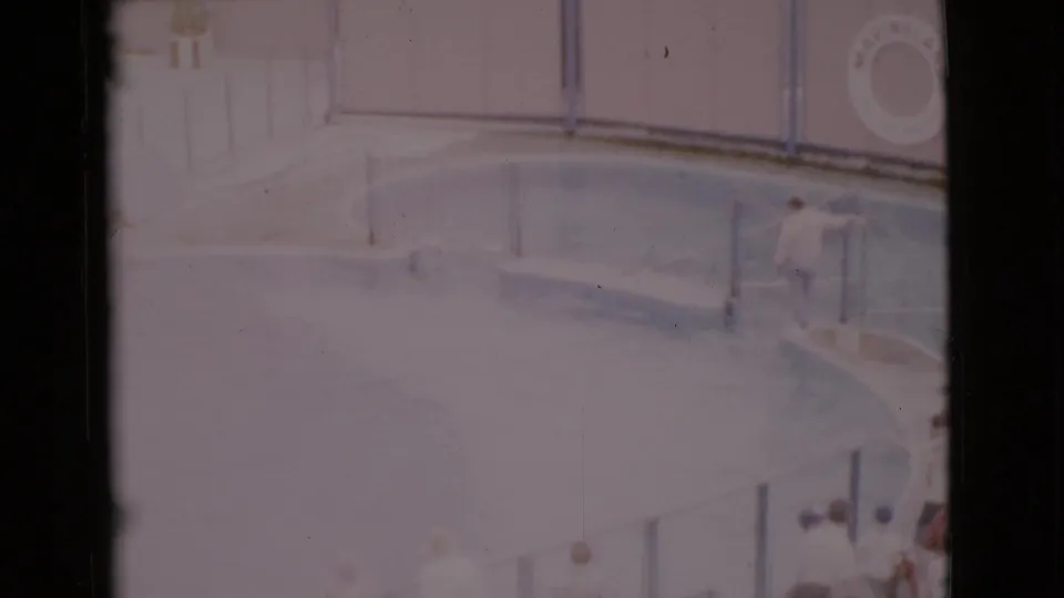 1968 San Diego County 8mm frame showing a circular pool, railings, diving board area, wall-mounted life preserver, and distant pool visitors.