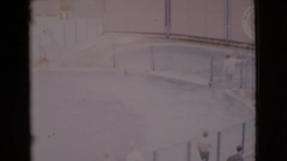 1968 San Diego County home-movie frame with a man at the pool edge, a circular pool, railings, life preserver, and nearby visitors.